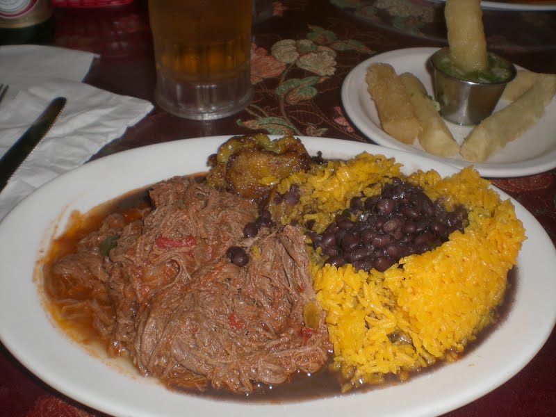 Typical Cuban dinner consisting of ropa vieja (shredded flank steak in a tomato sauce base), black beans, white rice, plantains and fried yucca. ? Photo by Marc Averette, Public domain, via Wikimedia Commons