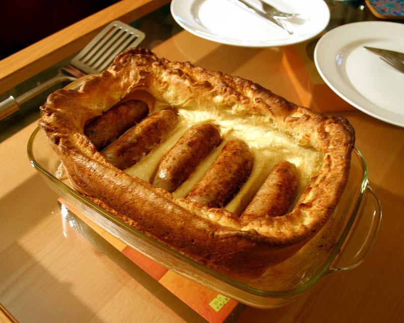 A cooked toad in the hole in a baking dish, on a table ready to serve. ? Photo by Robert Gibert, Public domain, via Wikimedia Commons