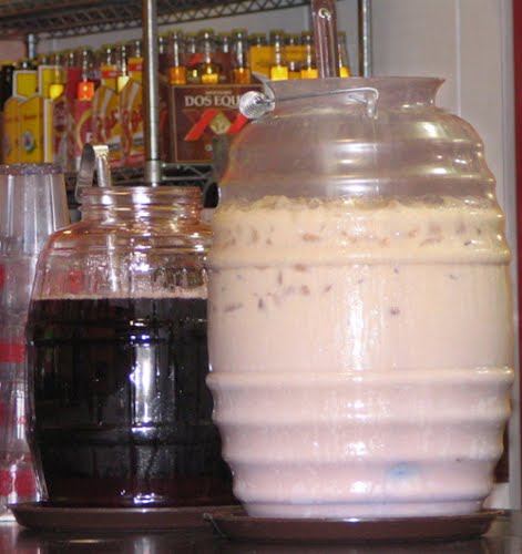 Photograph by ManekiNeko and released to the public domain. Two large jars of agua fresca in a Mexican restaurant in Seattle, Washington, USA. On the left is a jar of jamaica and on the right is a jar of horchata. Restaurant employees serve the drinks by ladling them from the jars into glasses. ? Photo by Original uploader was ManekiNeko at en.wikipedia, Public domain, via Wikimedia Commons